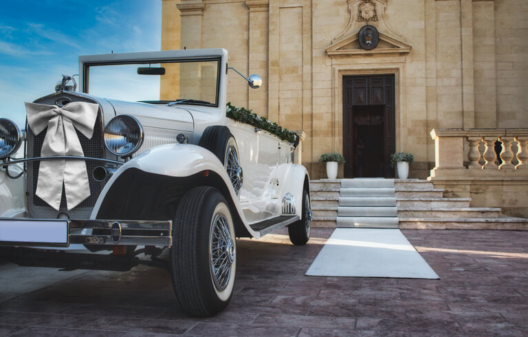 Weißer Oldtimer für eine traditionelle Hochzeit vor einer Kirche