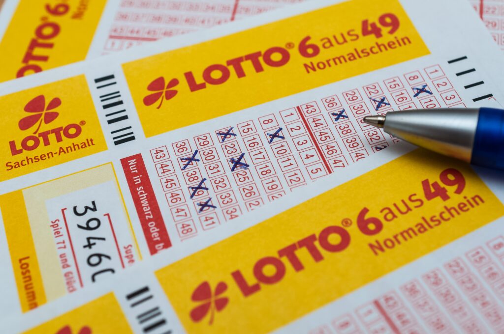 Ein ausgefüllter Lottoschein für "6 aus 49" von Lotto Sachsen-Anhalt, auf dem mehrere Felder mit blauen Kreuzen markiert sind. Ein blauer Stift zeigt auf den Schein.