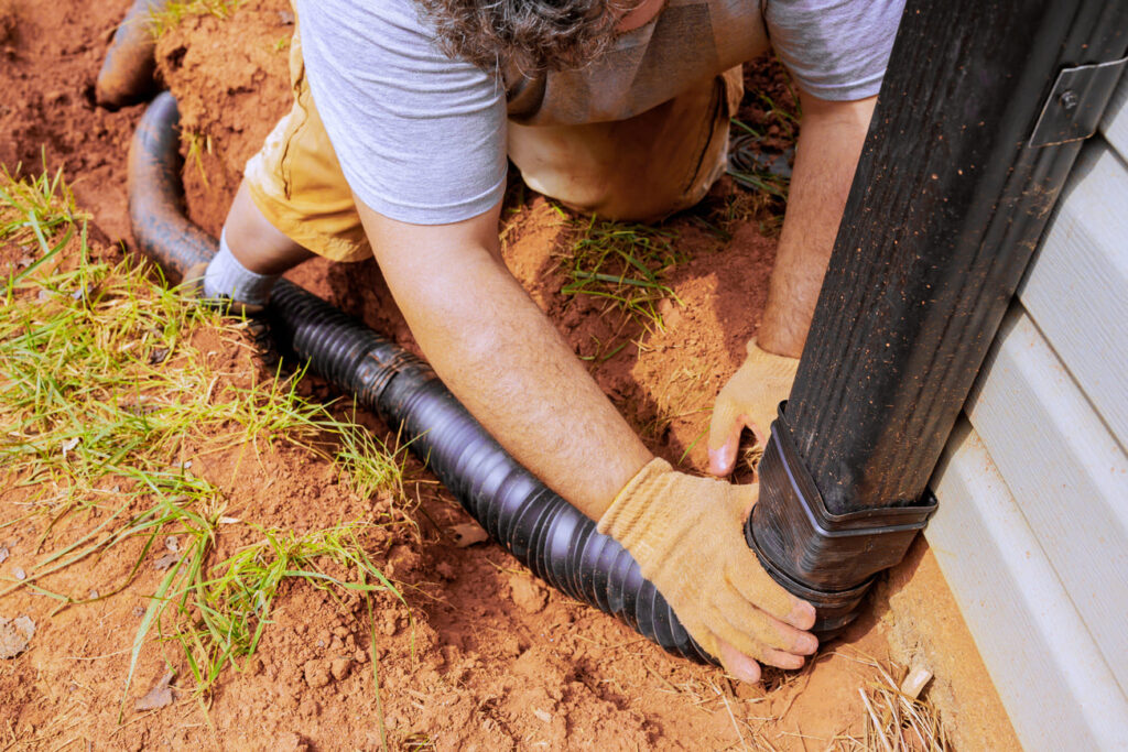 Ein Handwerker installiert ein Abflussrohr für die Zisterne zur Regenwassersammlung im Garten, um nachhaltige Wasserressourcen zu nutzen.