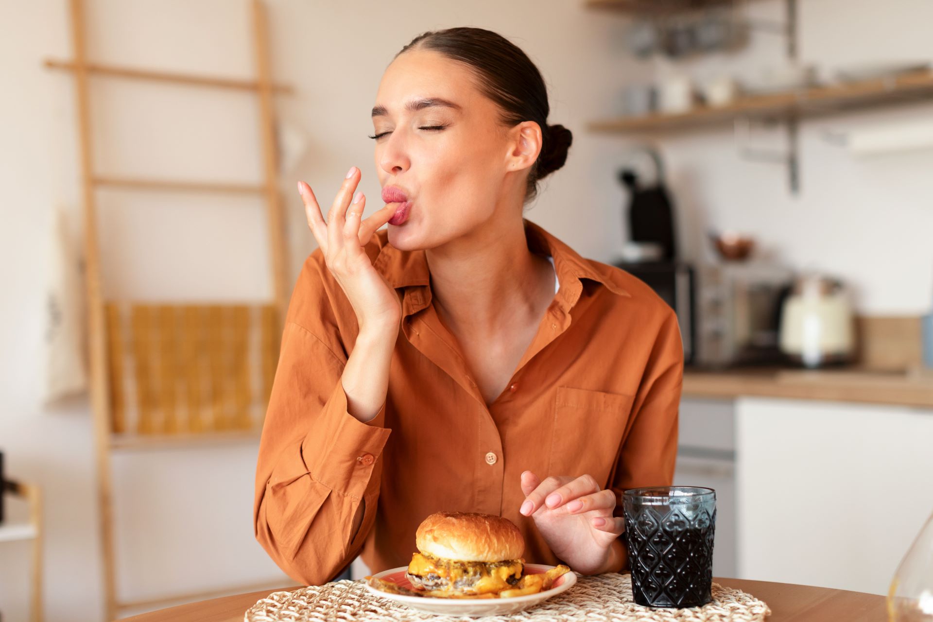 Eine Frau genießt einen Burger und leckt sich die Finger, ein Symbol für vollen Genuss und Zufriedenheit. Das Bild steht für bewusste Genussmomente im Alltag, die durch einfache, aber hochwertige Entscheidungen – wie mit 187 Pods – intensiviert werden können.