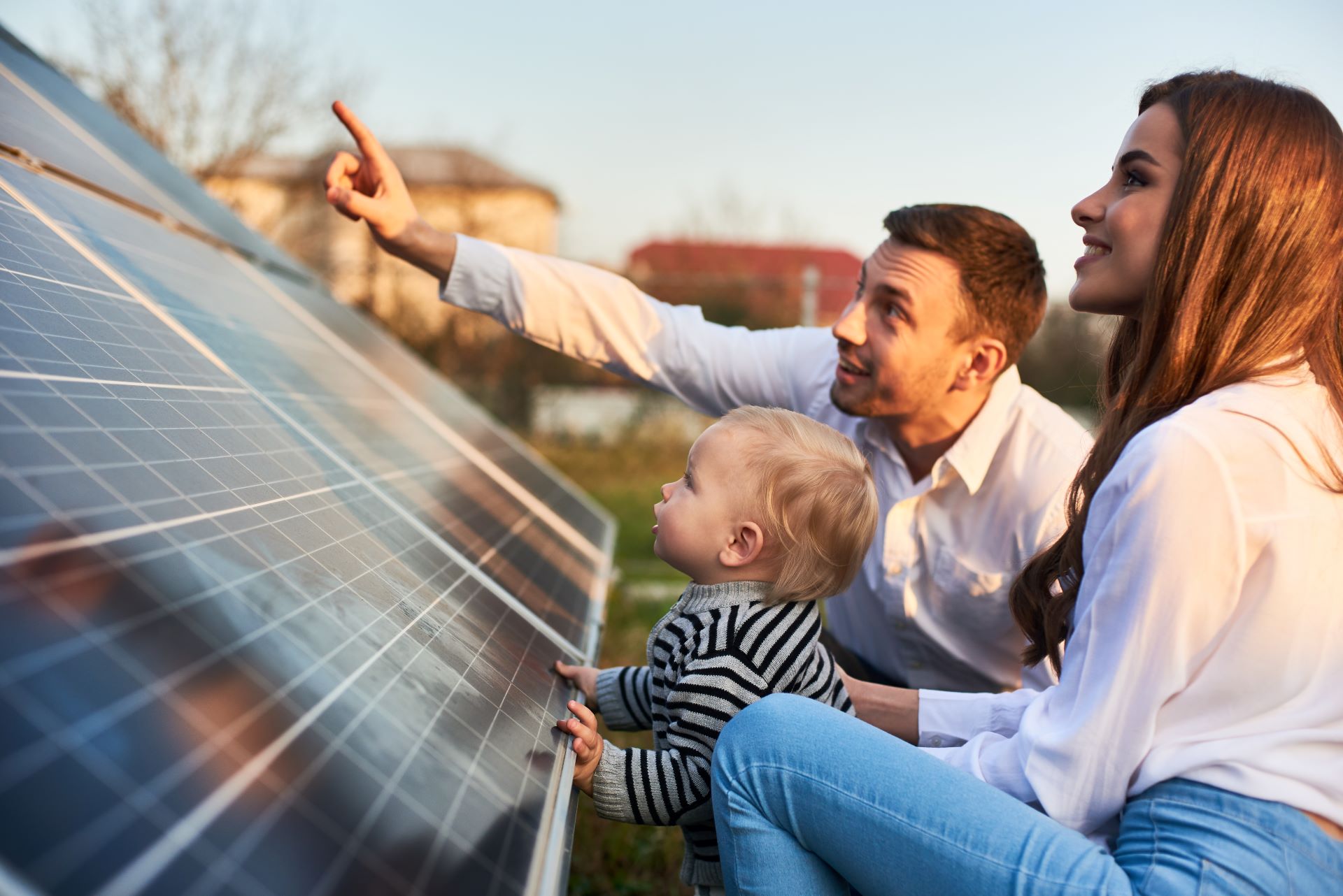 Junge Familie betrachtet Solarmodule auf ihrem Hausdach und diskutiert erneuerbare Energien.