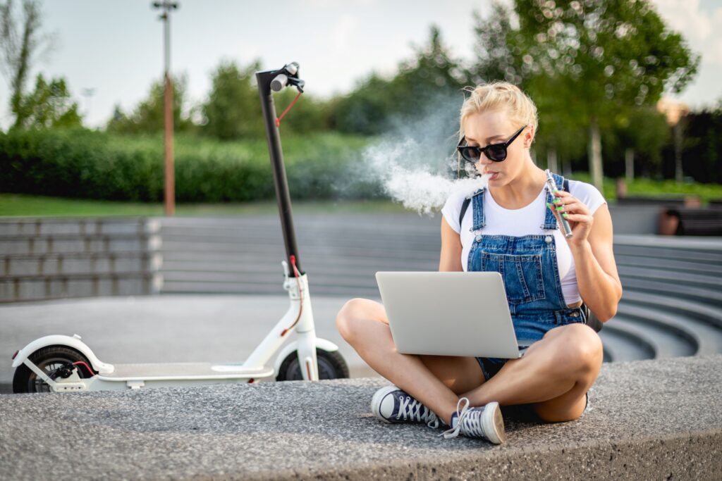 Eine Person sitzt draußen am rauchen und an einem Laptop