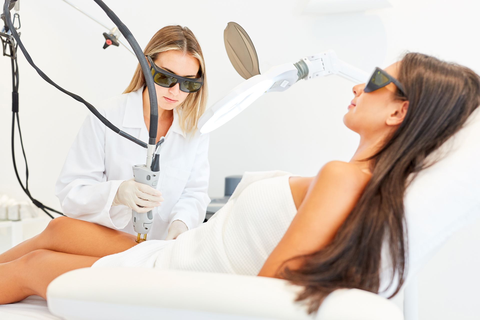 Professionelle Laser-Haarentfernung in einer Klinik, Fachkraft mit Schutzbrille behandelt eine Kundin auf einer Liege.