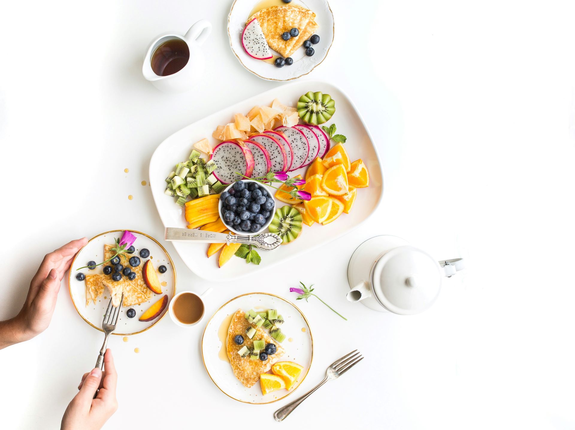 Stilvoll angerichteter Obstteller für Feinschmecker
Alternativtext: Ein farbenfroher Obstteller mit Drachenfrucht, Orangen, Kiwi und Heidelbeeren, umgeben von zwei Frühstückstellern mit Pfannkuchen.