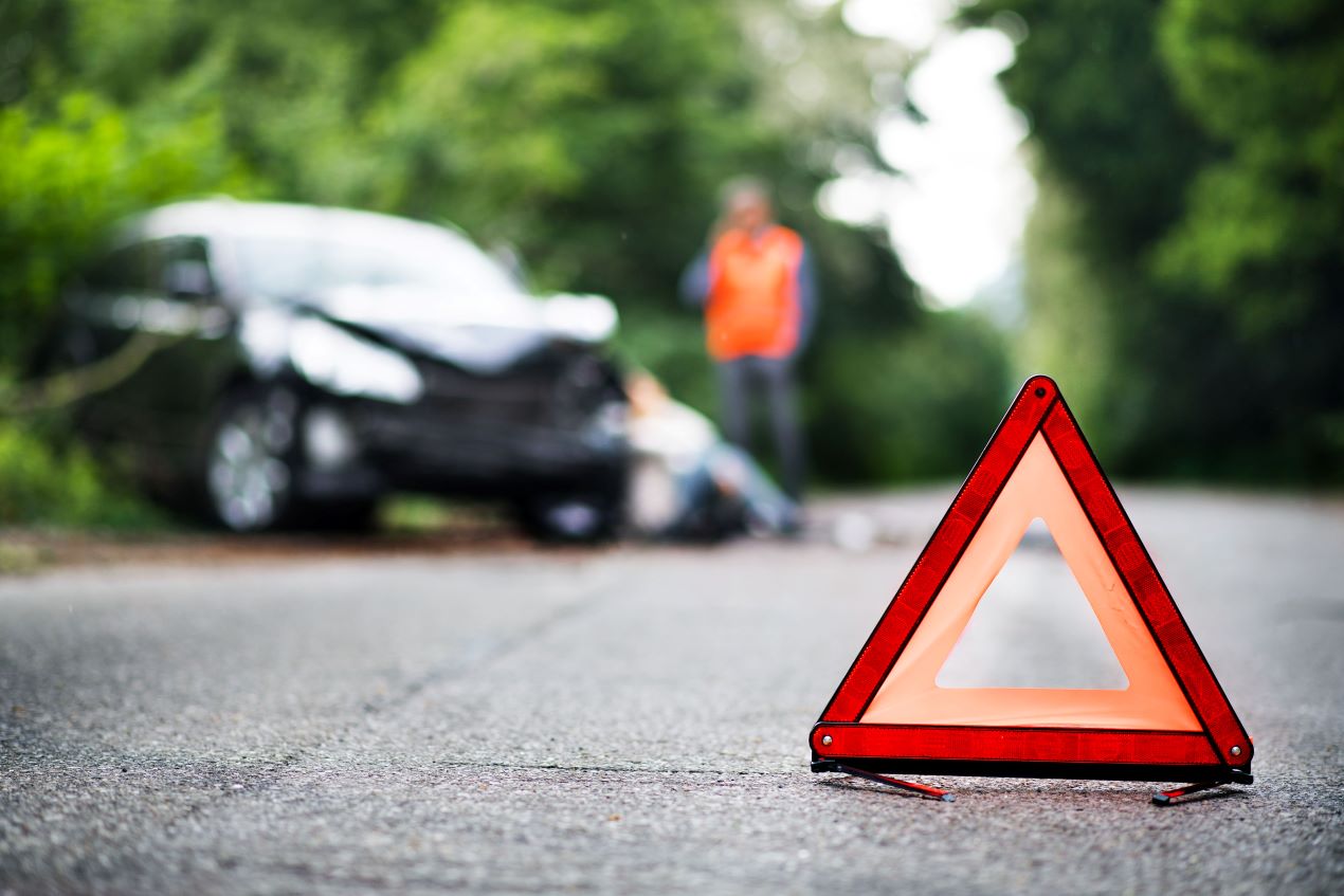 Ein Warndreieck auf der Straße vor einer Unfallstelle mit verletzter Person – Anwälte für Verkehrsrecht Mönchengladbach helfen bei rechtlichen Schritten nach einem Unfall.