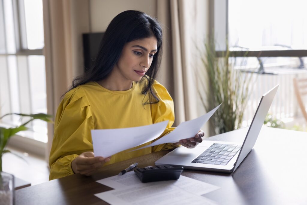 Junge Frau überprüft Lohnabrechnungen am Laptop – digitale Finanzverwaltung im Lohnbüro.