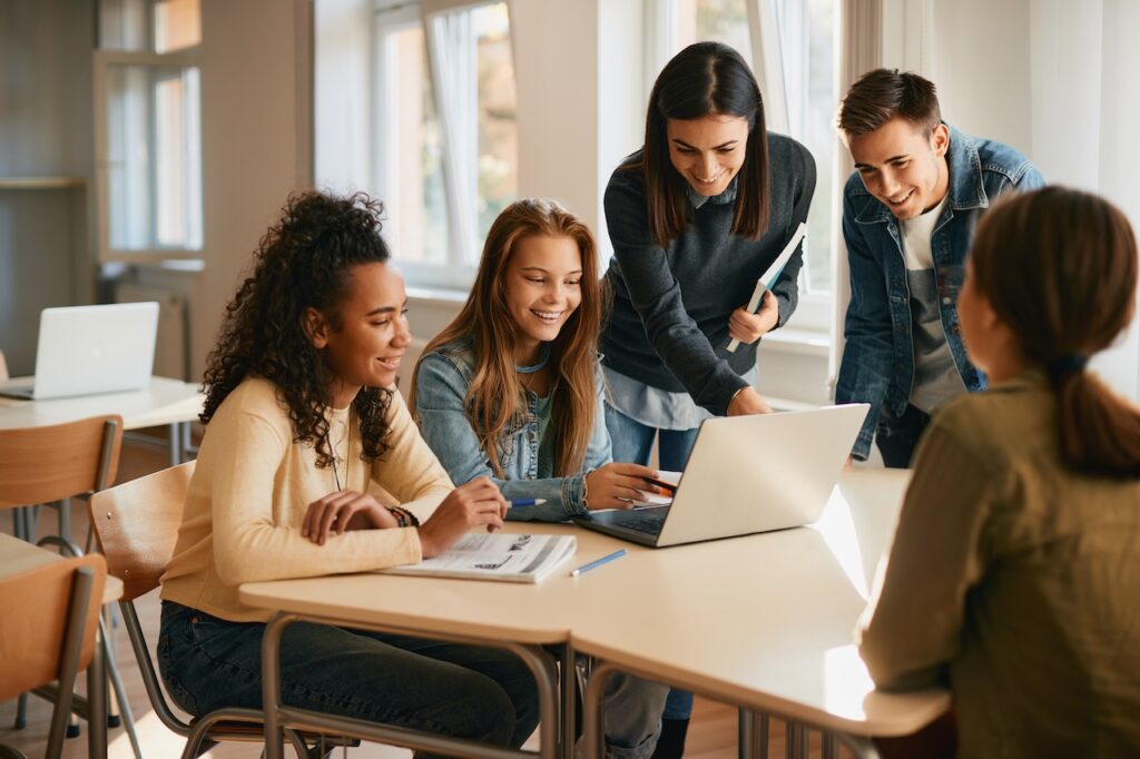 Schüler arbeiten gemeinsam an einem Laptop in einem hellen Klassenzimmer – digitales Lernen am privaten Gymnasium Berlin.