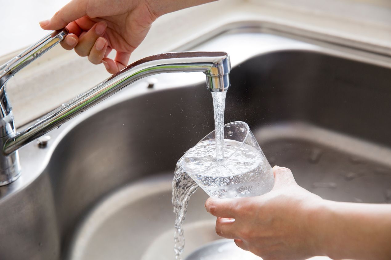Hand füllt ein Trinkglas mit Leitungswasser aus dem Wasserhahn dank installierter Entkalkungsanlage in der Küche