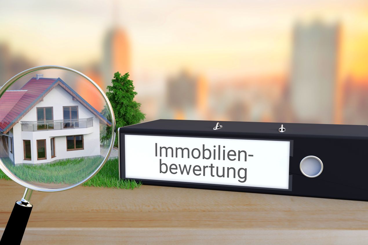 Modellhaus unter Lupe neben Aktenordner mit Aufschrift Immobilienbewertung – Symbolbild für sorgfältige Immobilienbewertung Reutlingen