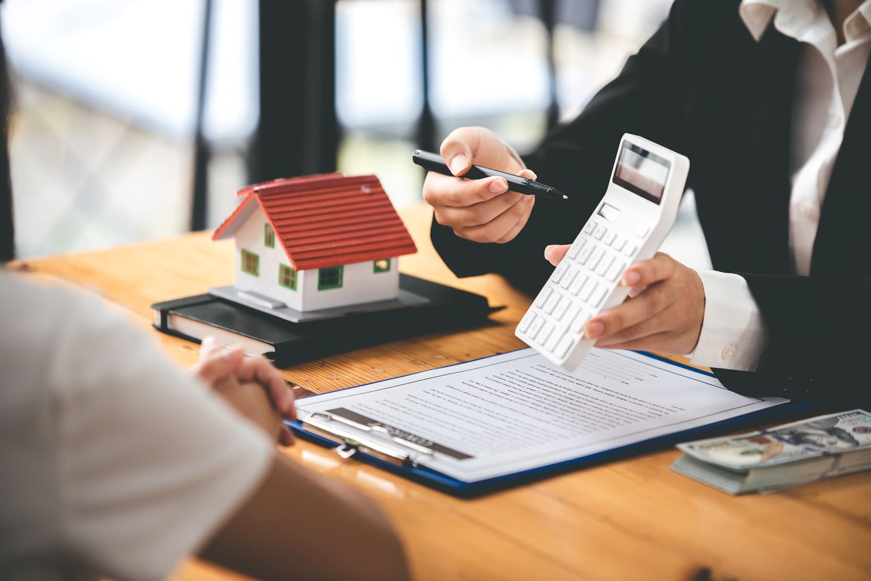 Immobilienberaterin erklärt Kaufpreis mit Taschenrechner und Modellhaus – persönliche Beratung zur Immobilienbewertung Reutlingen am Tisch