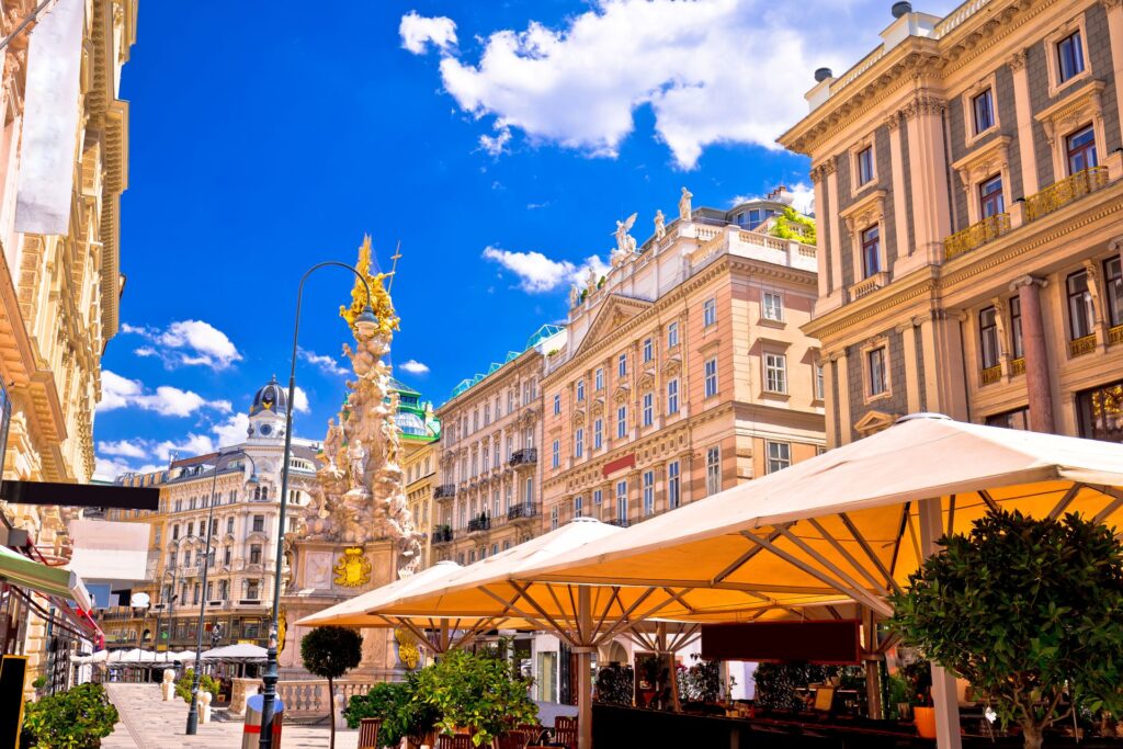 Wiener Graben mit Pestsaeule und Straßencafé bei blauem Himmel